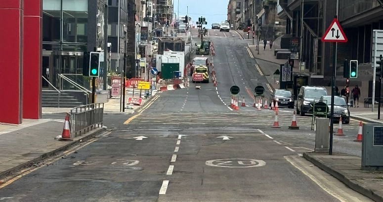 View of reopened double lane road. Buildings can be seen on either side and vehicles up ahead.