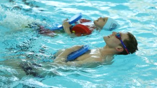 Duncan Scott pictured in the swimming pool beside a child. They are both holding a float while swimming backwards.