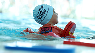 Learn to Swim Design a Cap Competition back view of young child in swimming pool with red float, wearing Learn to Swim cap