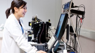 Scientist in lab coat using a laptop with advanced laboratory equipment in the background. Scientist in lab coat using a laptop with advanced laboratory equipment in the background.