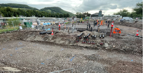 View of construction site with excavation in the foreground and workers in high viz in the background