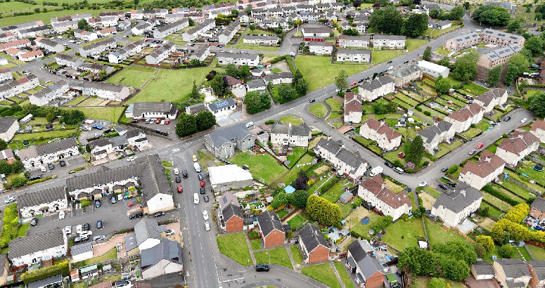 Drone image of residential area showing houses, roads, and green spaces.