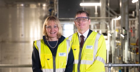 Two people smiling inside large building with pipework infrastructure