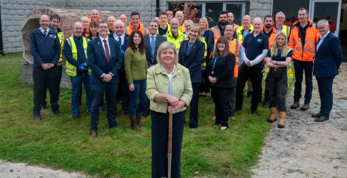 Large group of people smiling in front of concrete building while wearing hi-vis and safety PPE