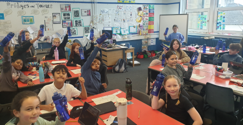 Students raising water bottles in a classroom filled with educational posters