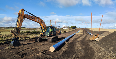 Network pipes laid out on the ground with yellow digger